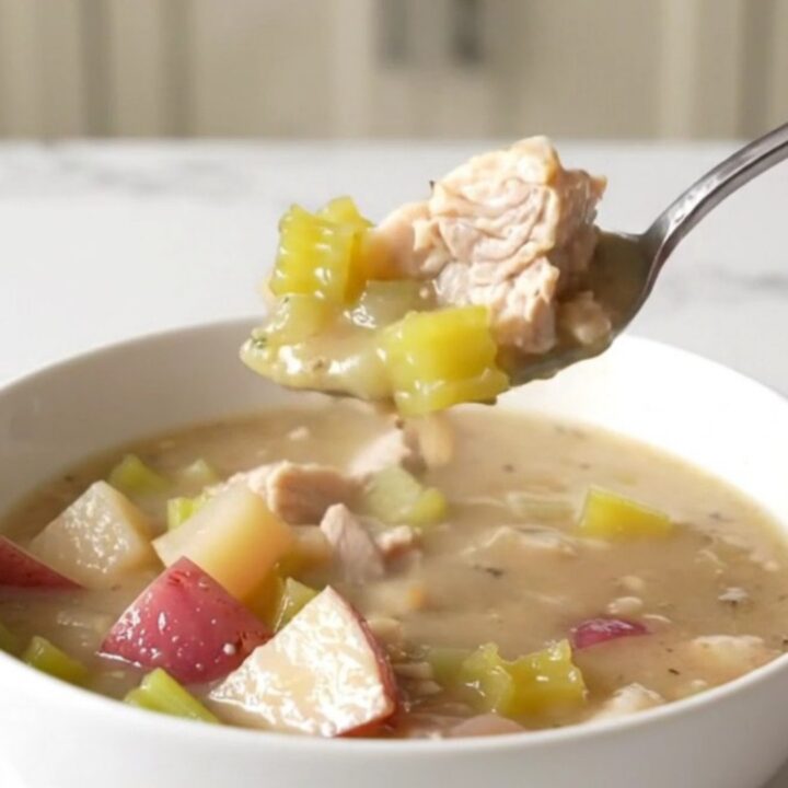 A bowl of creamy chicken and potato chowder with visible chunks of chicken, red potatoes, and celery.