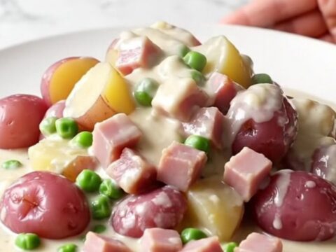 A rustic, close-up shot of a white plate filled with creamy diced ham, baby red potatoes