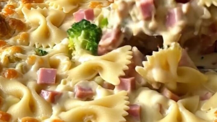 A top-down view of a creamy bowtie pasta bake with ham and broccoli in a white ceramic dish.