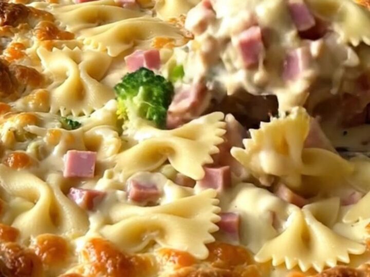 A top-down view of a creamy bowtie pasta bake with ham and broccoli in a white ceramic dish.