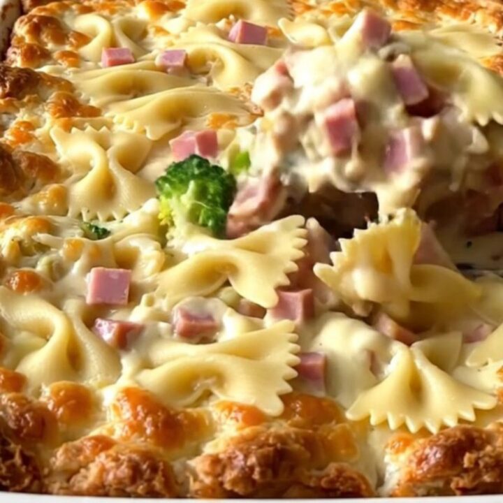 A top-down view of a creamy bowtie pasta bake with ham and broccoli in a white ceramic dish.