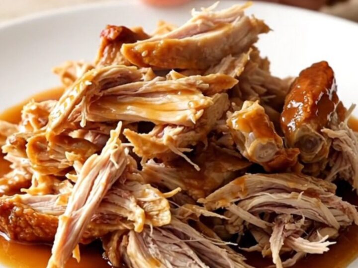 A close-up of tender, shredded Carolina-style pulled chicken in a vibrant vinegar barbecue sauce.
