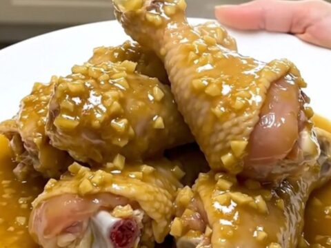 A close-up of tender chicken drumsticks and baby carrots in a rich garlic gravy inside a slow cooker.