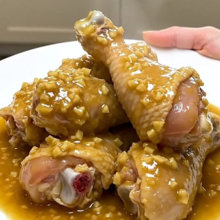 A close-up of tender chicken drumsticks and baby carrots in a rich garlic gravy inside a slow cooker.