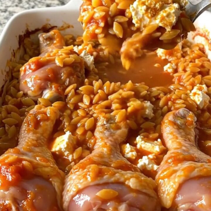 A top-down view of a rectangular baking dish filled with roasted chicken drumsticks and tomato orzo topped with feta.