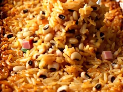 A large white enameled baker filled with cooked Hoppin' John rice, peas, ham, and green onions.