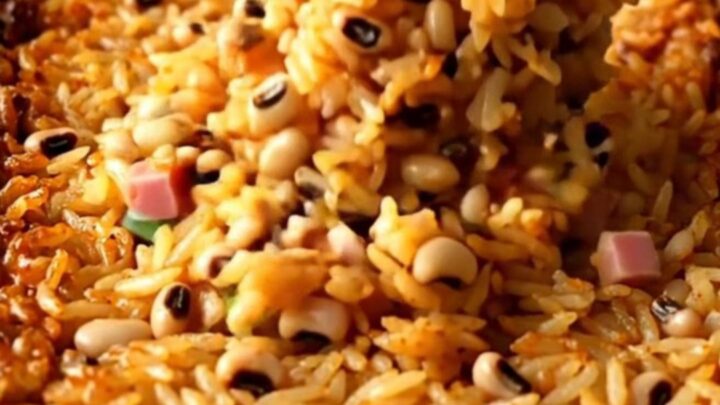 A large white enameled baker filled with cooked Hoppin' John rice, peas, ham, and green onions.