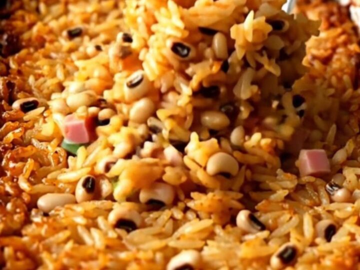 A large white enameled baker filled with cooked Hoppin' John rice, peas, ham, and green onions.