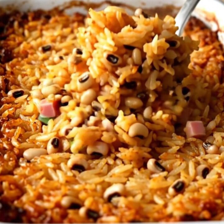 A large white enameled baker filled with cooked Hoppin' John rice, peas, ham, and green onions.