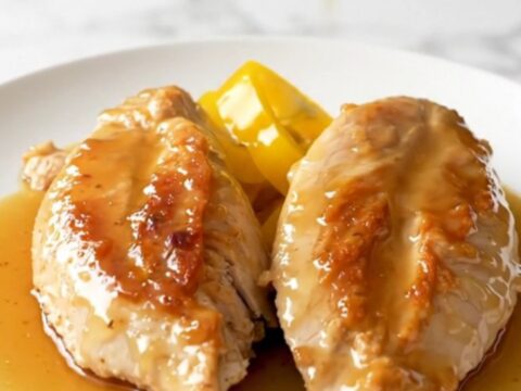 A close-up of tender, slow-cooked chicken breasts topped with bright yellow banana pepper rings and a glossy honey glaze