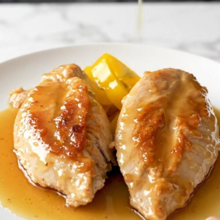 A close-up of tender, slow-cooked chicken breasts topped with bright yellow banana pepper rings and a glossy honey glaze