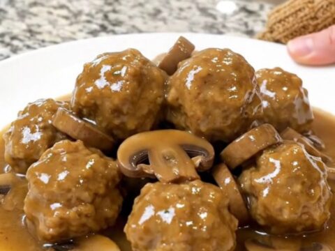 A close-up of chicken meatballs in a creamy mushroom gravy inside a matte black slow cooker.