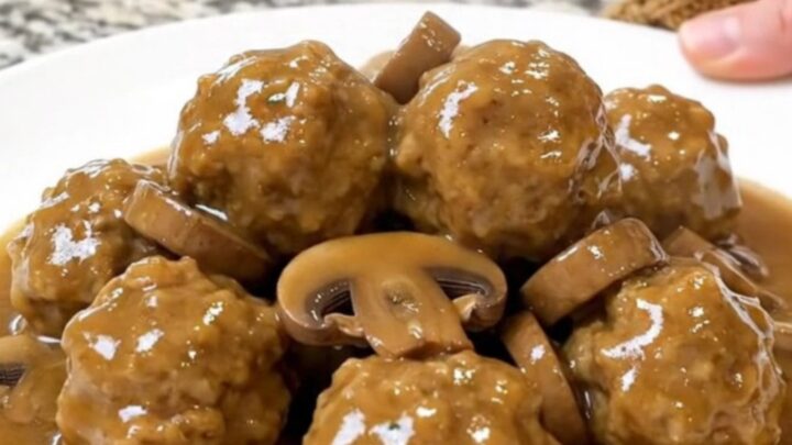 A close-up of chicken meatballs in a creamy mushroom gravy inside a matte black slow cooker.