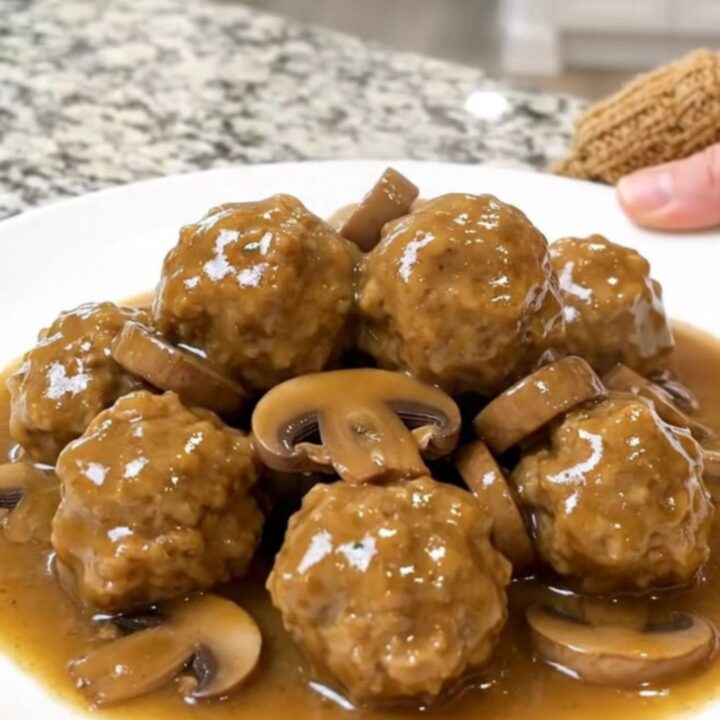 A close-up of chicken meatballs in a creamy mushroom gravy inside a matte black slow cooker.