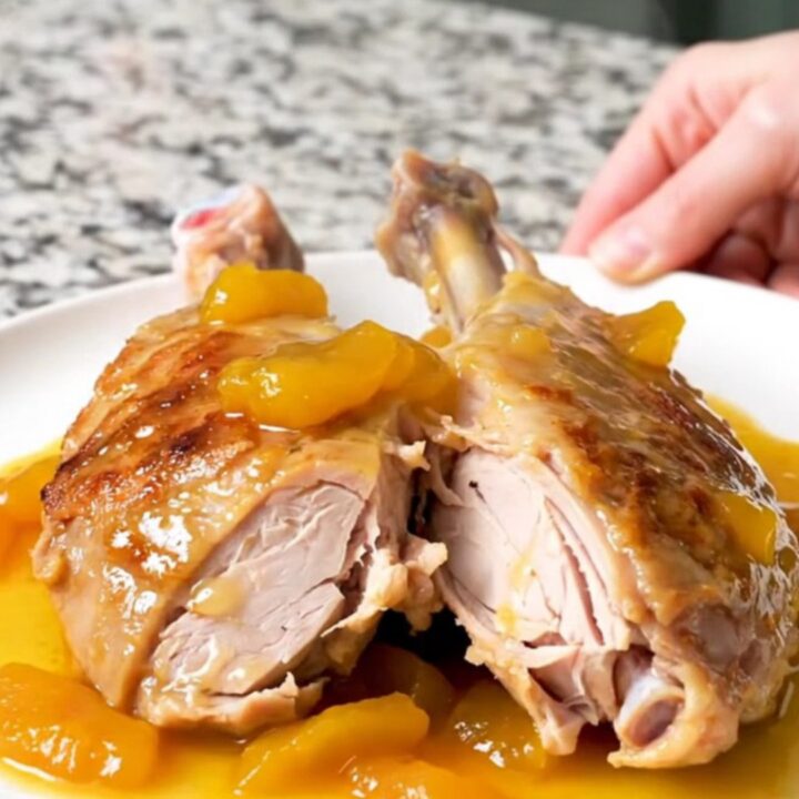 A whole, slow-cooked turkey tenderloin covered in a glossy, golden-brown apricot sauce on a white plate.