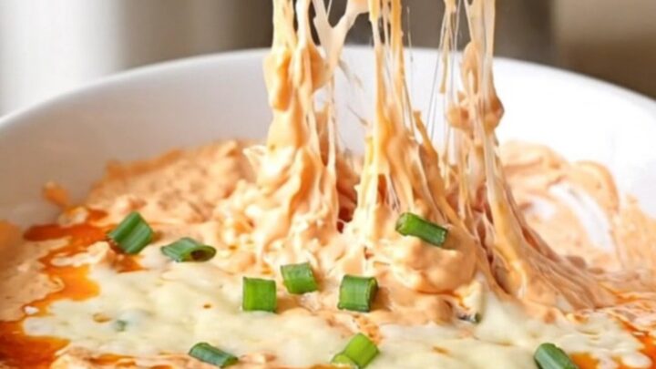 A close-up of creamy chicken rangoon dip in a slow cooker with visible melted cheese and green onions.
