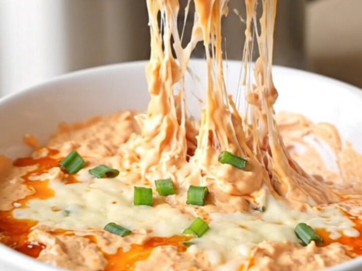 A close-up of creamy chicken rangoon dip in a slow cooker with visible melted cheese and green onions.