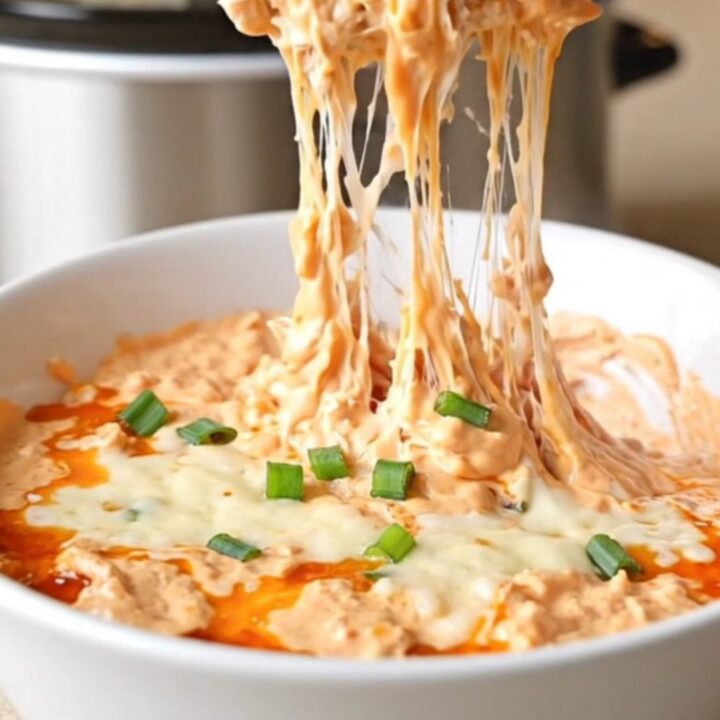 A close-up of creamy chicken rangoon dip in a slow cooker with visible melted cheese and green onions.