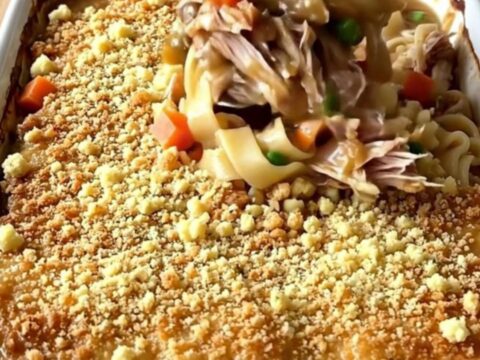 A large rectangular baking dish filled with a golden-brown turkey and noodle bake on a butcher-block counter.