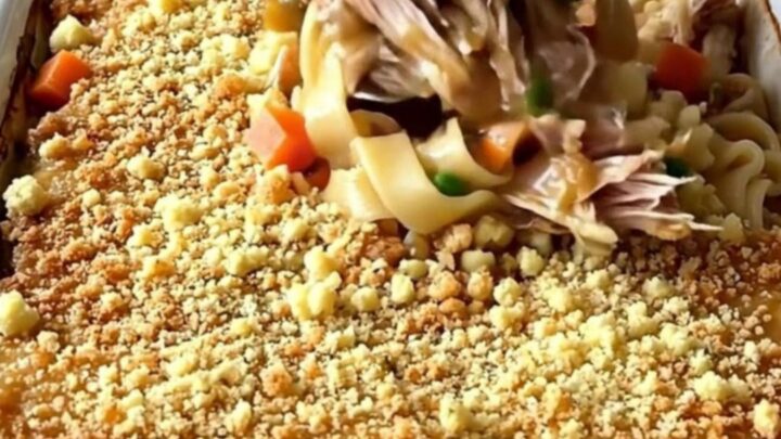 A large rectangular baking dish filled with a golden-brown turkey and noodle bake on a butcher-block counter.