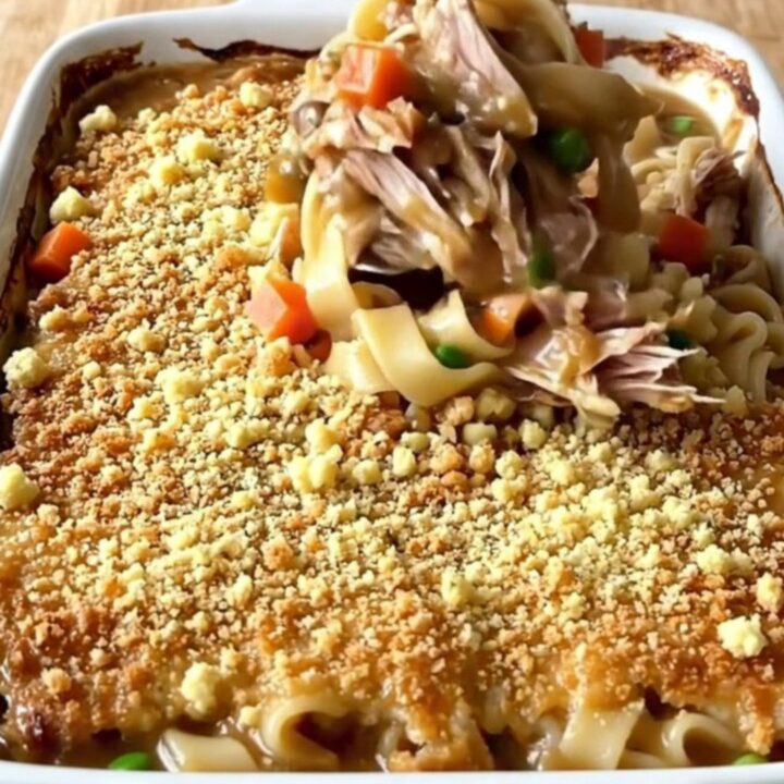 A large rectangular baking dish filled with a golden-brown turkey and noodle bake on a butcher-block counter.