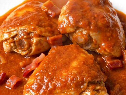 A rustic slow cooker filled with tender chicken thighs, crispy bacon, and soft onions in a rich, smoky tomato sauce.