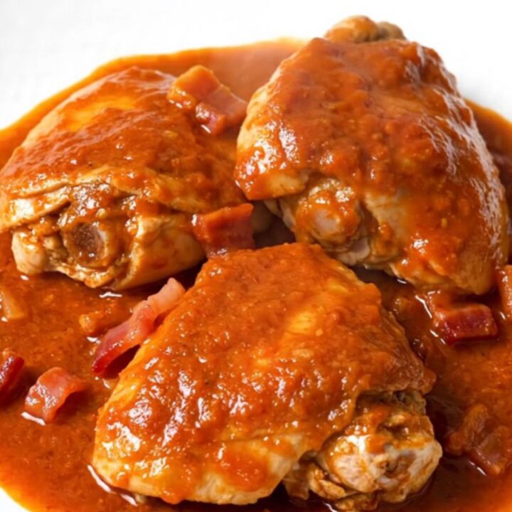 A rustic slow cooker filled with tender chicken thighs, crispy bacon, and soft onions in a rich, smoky tomato sauce.