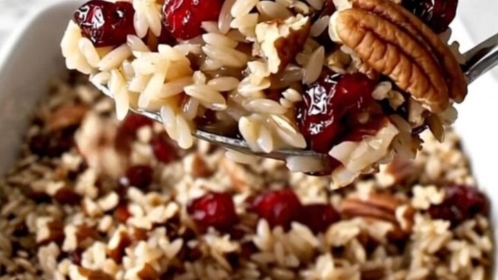 A rectangular ceramic dish filled with cooked wild rice, bright red cranberries, and toasted pecans.