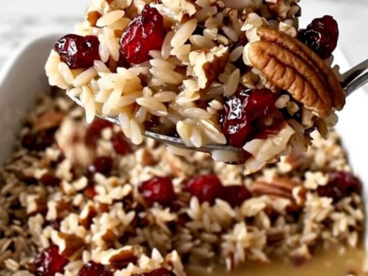 A rectangular ceramic dish filled with cooked wild rice, bright red cranberries, and toasted pecans.