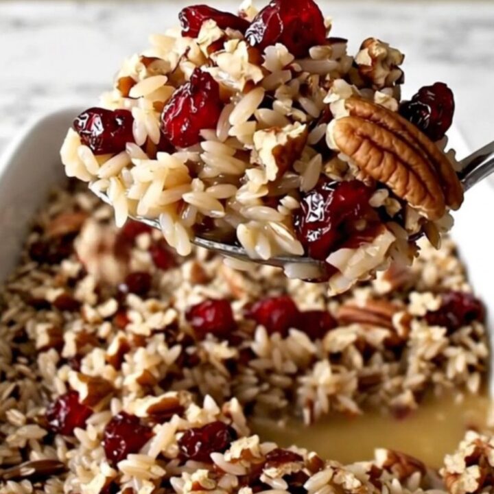 A rectangular ceramic dish filled with cooked wild rice, bright red cranberries, and toasted pecans.