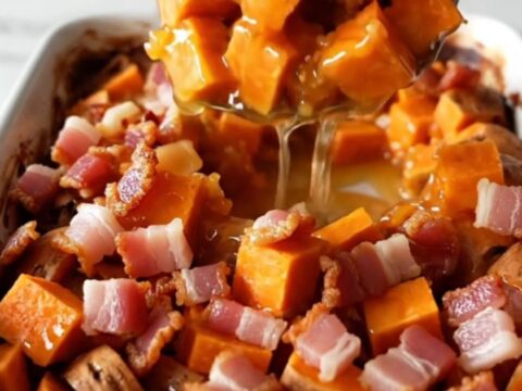 A golden, caramelized sweet potato bake in a white ceramic dish with crispy bacon pieces on top.