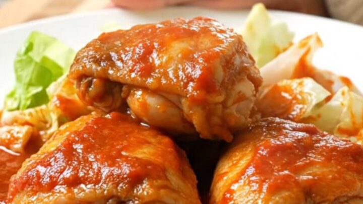 A slow cooker filled with chicken thighs and cabbage wedges in a rich, vibrant red tomato sauce.