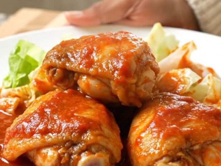 A slow cooker filled with chicken thighs and cabbage wedges in a rich, vibrant red tomato sauce.
