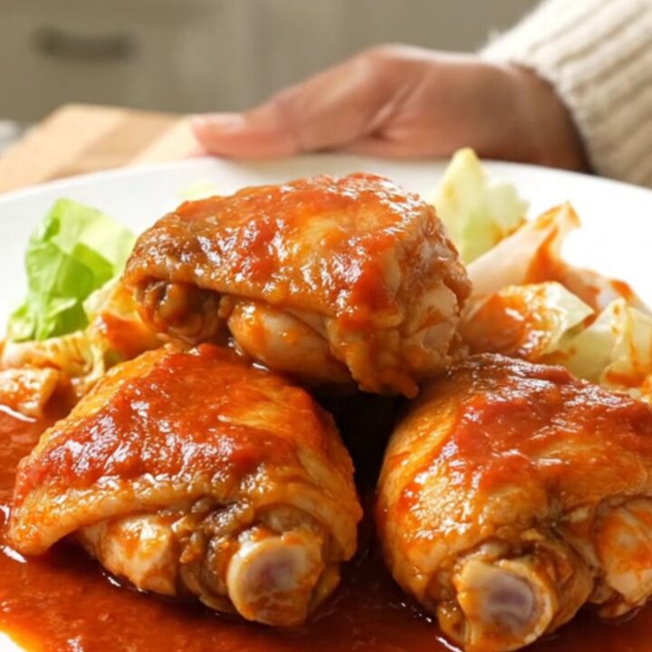 A slow cooker filled with chicken thighs and cabbage wedges in a rich, vibrant red tomato sauce.
