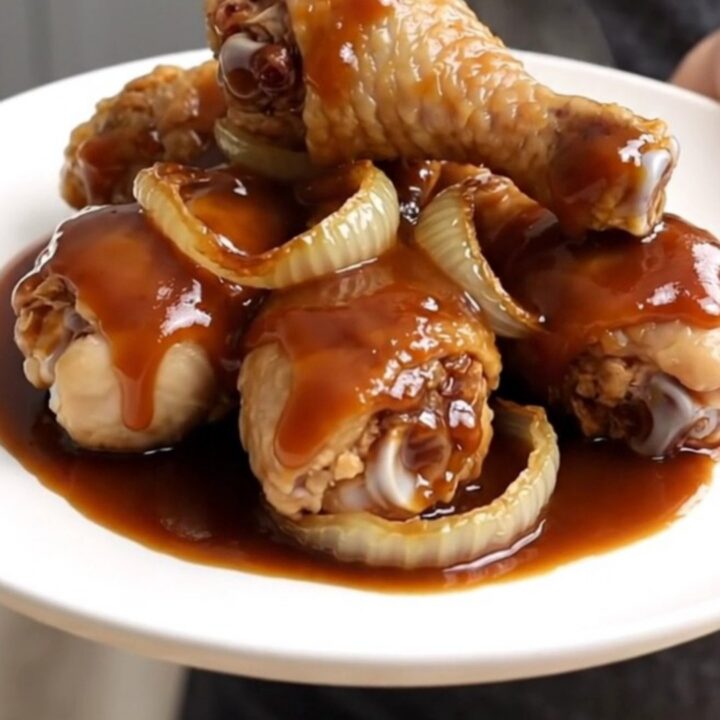 Close-up view of cooked cola-glazed chicken drumsticks arranged neatly on a white plate.