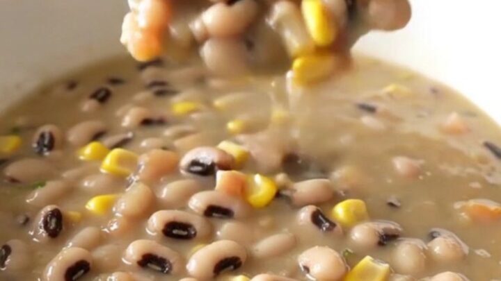 A bowl of creamy cowboy caviar soup served in a white bowl with steam rising, featuring visible beans, corn, and peppers.