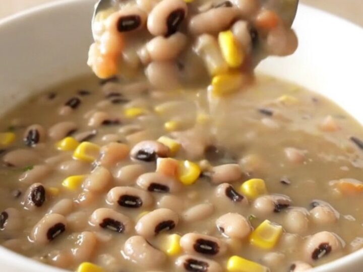 A bowl of creamy cowboy caviar soup served in a white bowl with steam rising, featuring visible beans, corn, and peppers.