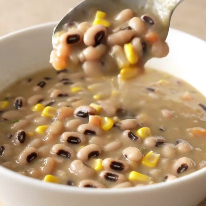 A bowl of creamy cowboy caviar soup served in a white bowl with steam rising, featuring visible beans, corn, and peppers.