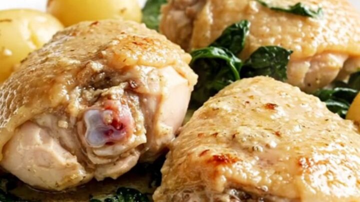 A slow cooker filled with creamy chicken thighs, artichoke hearts, and baby potatoes in a white sauce.