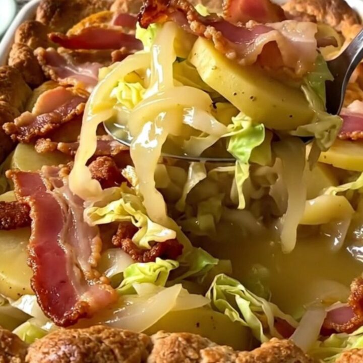 A rectangular ceramic dish filled with layers of tender cabbage, sliced gold potatoes, and crispy bacon.