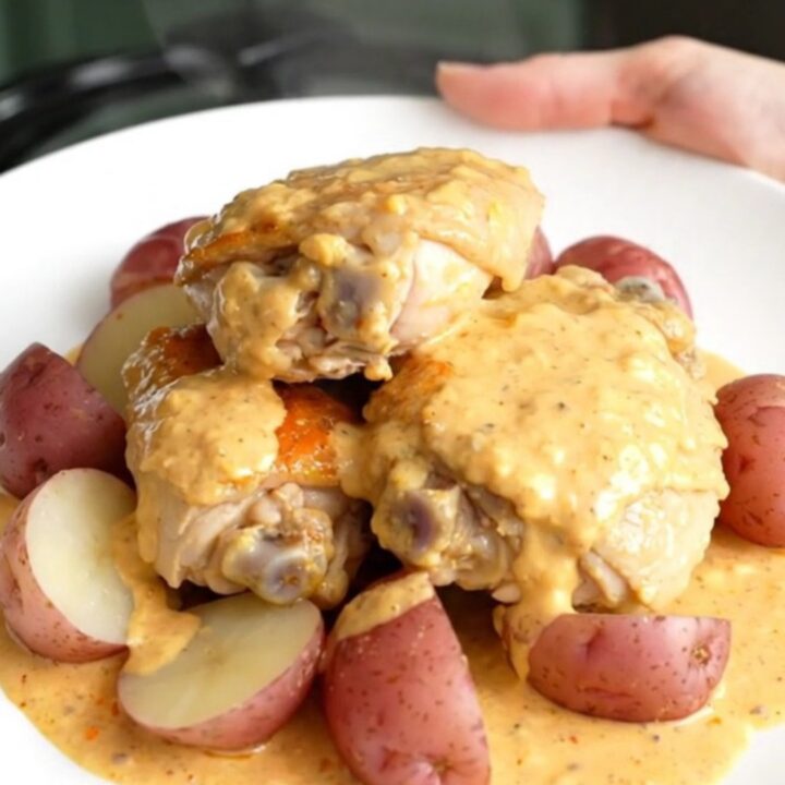 A close-up of creamy Chesapeake chicken thighs and baby red potatoes served on a white plate.