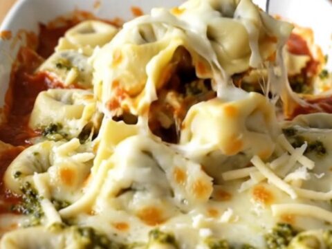 A large rectangular ceramic baking dish filled with baked cheese tortellini topped with melted mozzarella and pesto swirls.