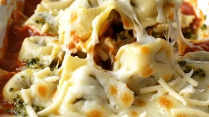 A large rectangular ceramic baking dish filled with baked cheese tortellini topped with melted mozzarella and pesto swirls.