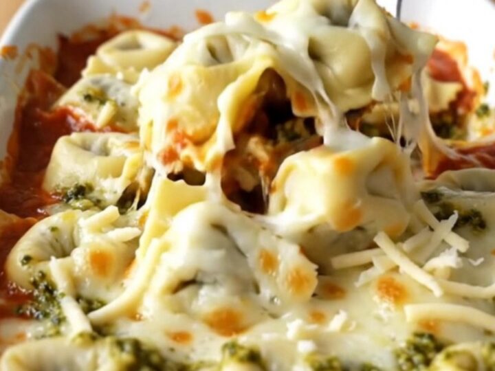 A large rectangular ceramic baking dish filled with baked cheese tortellini topped with melted mozzarella and pesto swirls.