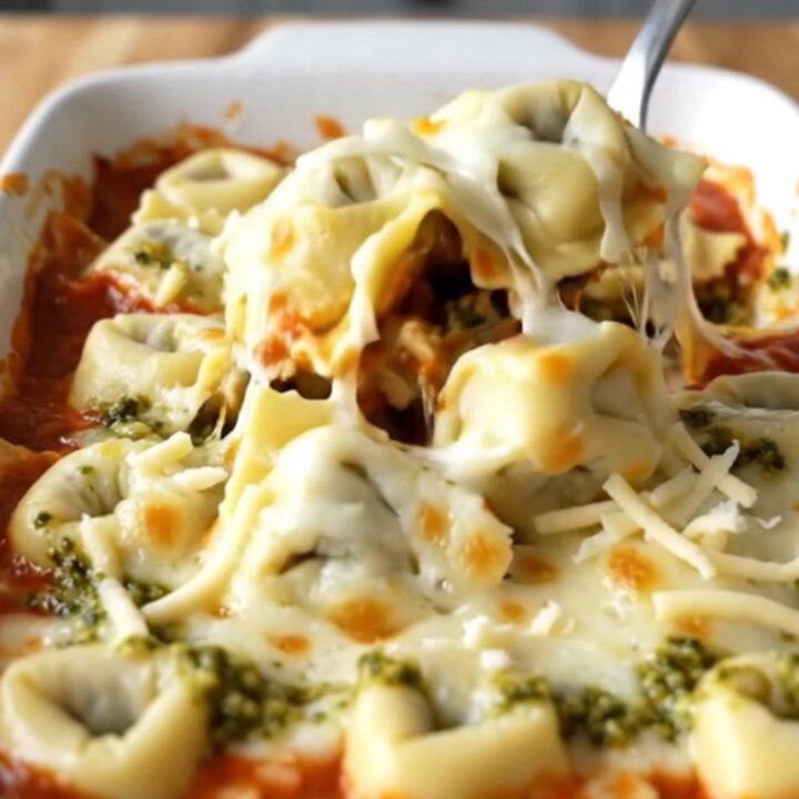 A large rectangular ceramic baking dish filled with baked cheese tortellini topped with melted mozzarella and pesto swirls.