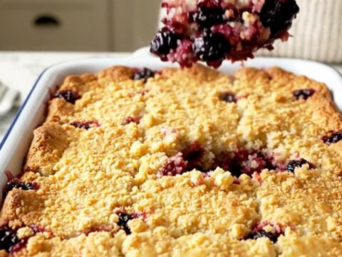 A warm blueberry lemon dump cake in a white rectangular baking dish with a golden crust and bubbling berries.