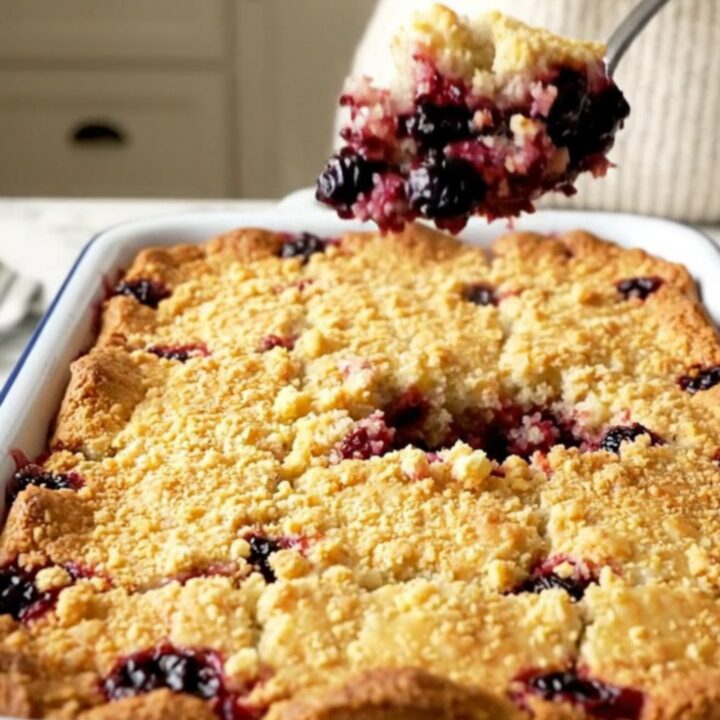 A warm blueberry lemon dump cake in a white rectangular baking dish with a golden crust and bubbling berries.