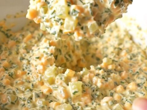 A creamy, warm slow cooker fried pickle dip in a white bowl with a spoon, showing melted cheese and pickle bits.