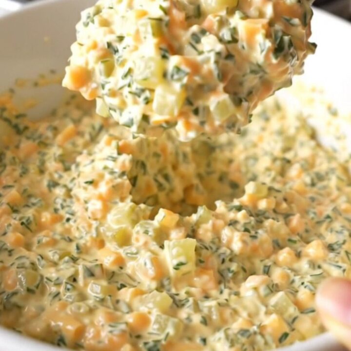 A creamy, warm slow cooker fried pickle dip in a white bowl with a spoon, showing melted cheese and pickle bits.