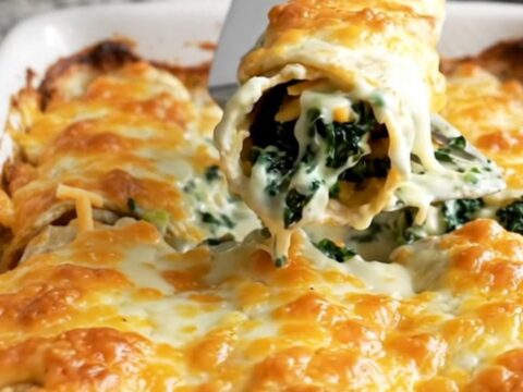 A top-down view of a rectangular ceramic baking dish filled with spinach and cheese enchiladas covered in white sauce.